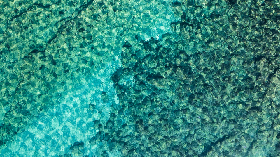 Underwater view of rocks and sand with light reflections in turquoise water