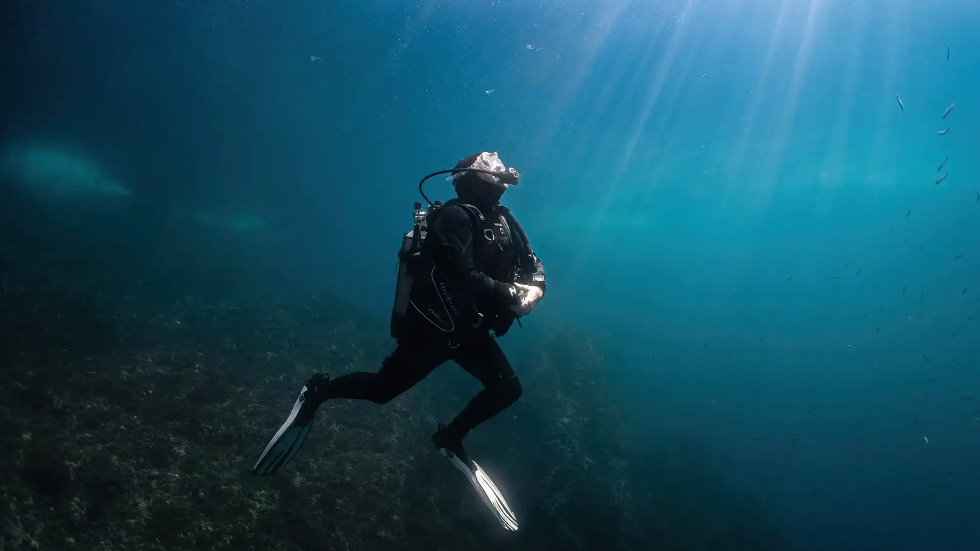 Plongeur en scaphandre évoluant sous l'eau avec des rayons de soleil filtrant à travers la surface